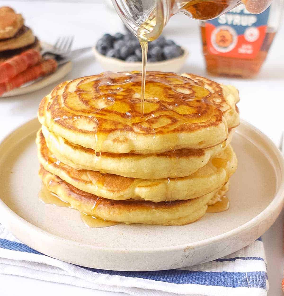 Maple syrup being poured over a stack of sourdough pancakes in a plate.
