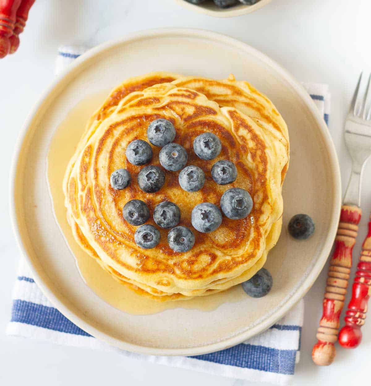 A stack of pancakes on a plate with blueberries on top.