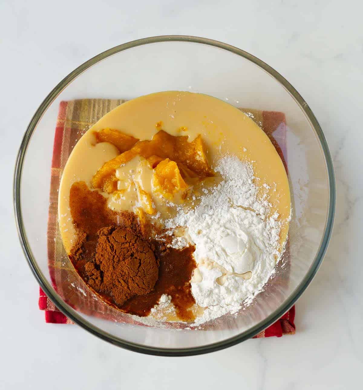 Ingredients for pumpkin pie filling in a glass mixing bowl.