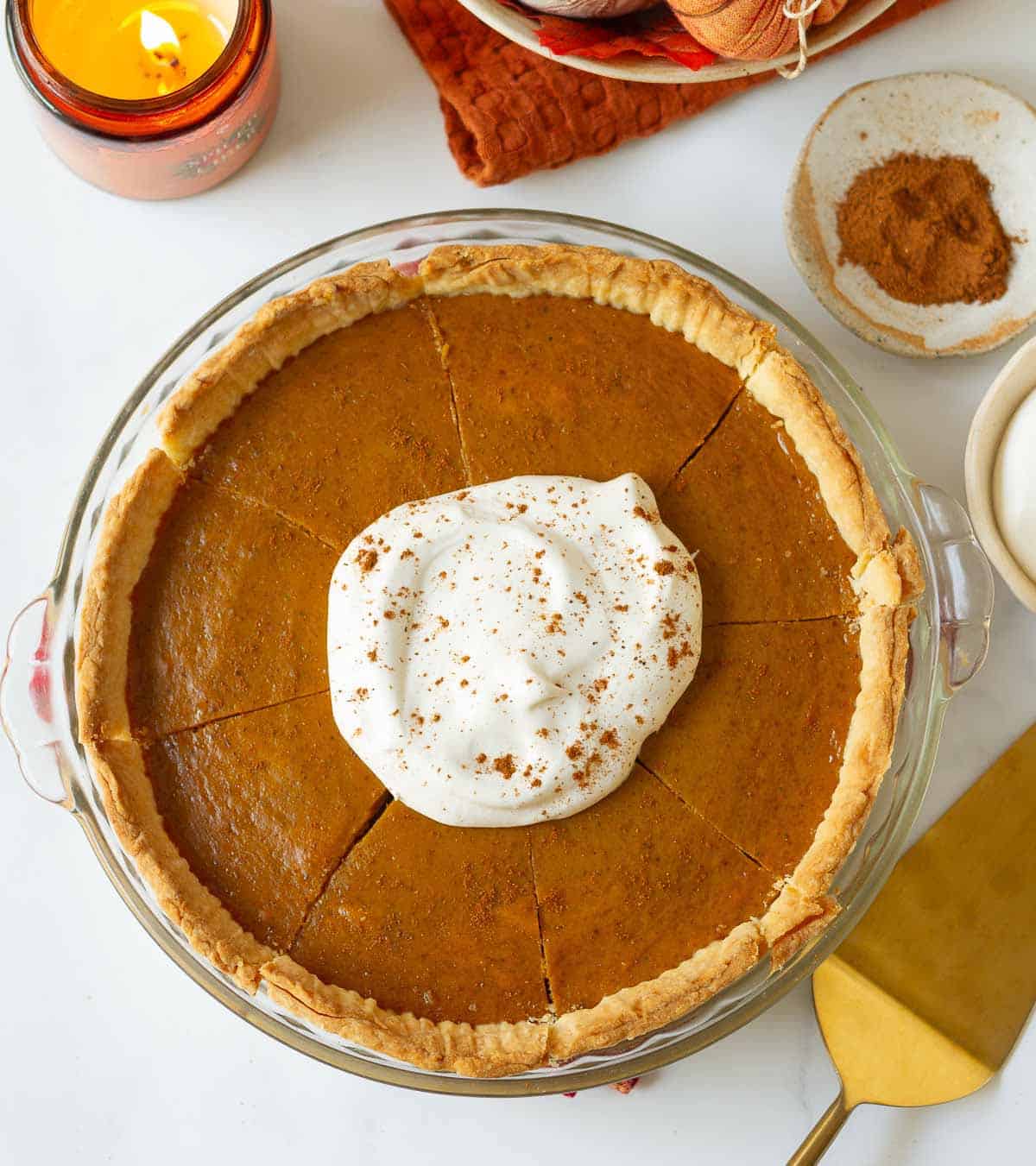 Eggless pumpkin pie with whipped cream and pie spice on top with candle and spices around.