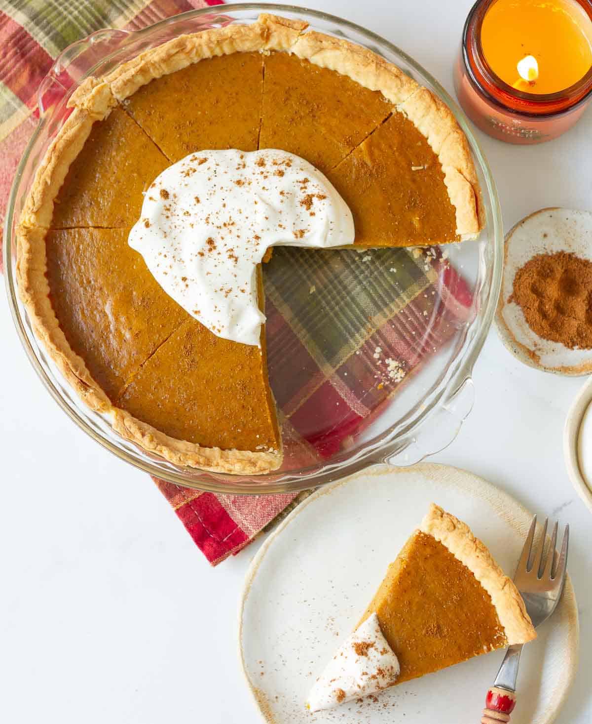 Sliced pumpkin pie topped with whipped cream with a slice on a plate.
