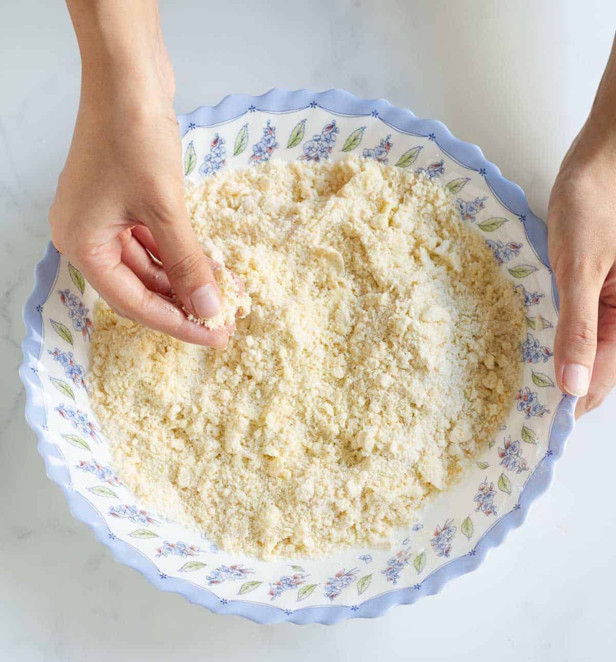 A hand rubbing the butter and flour in a mixing bowl.