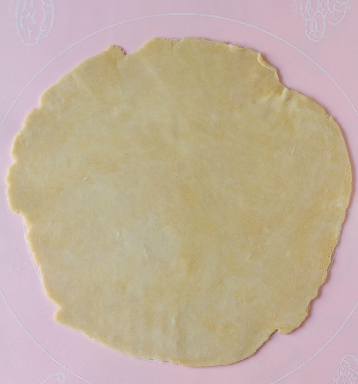 Rolled out pastry dough on a pink silicone mat.