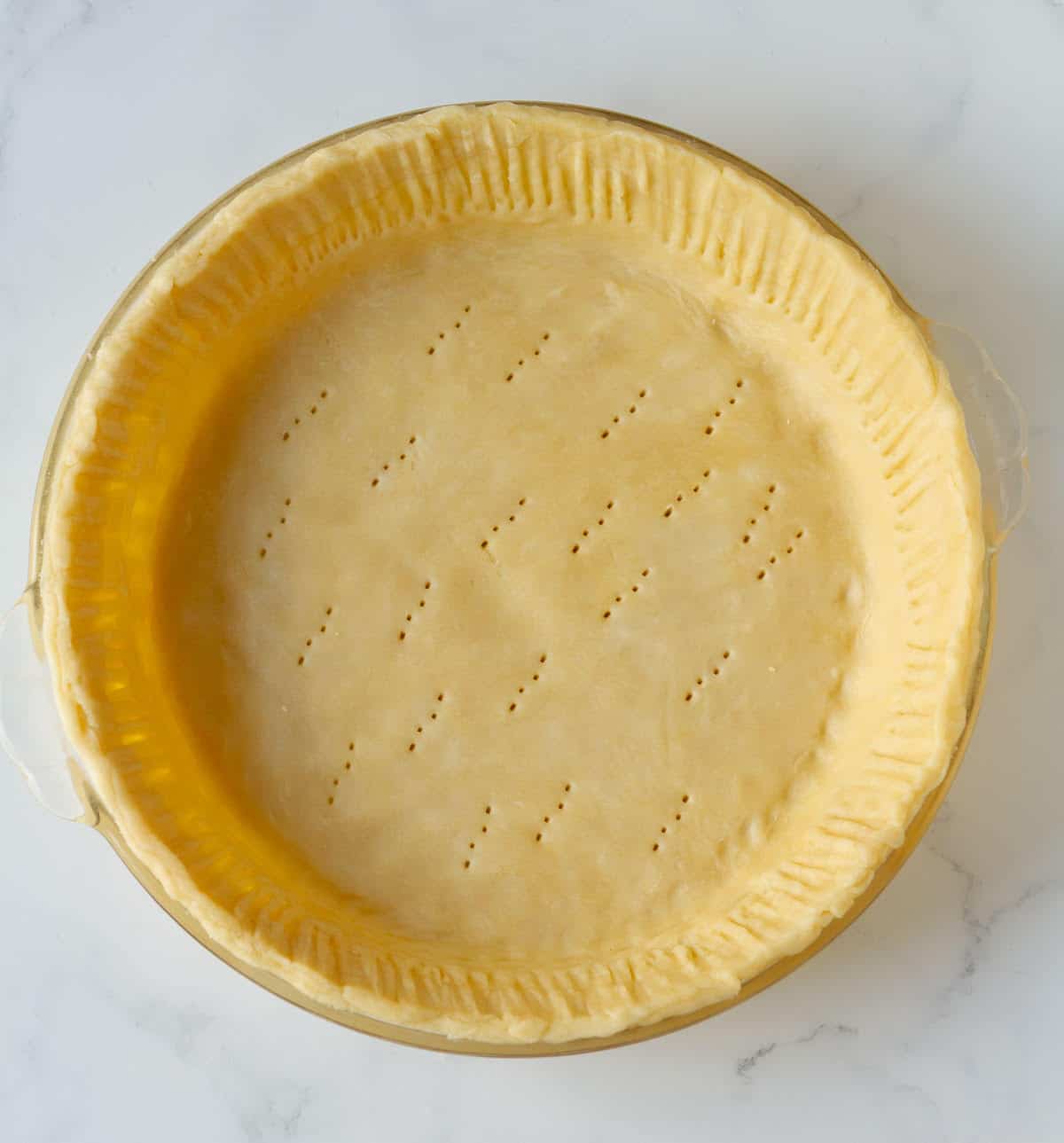 Pastry dough in a pie plate with holes pricked in the bottom.
