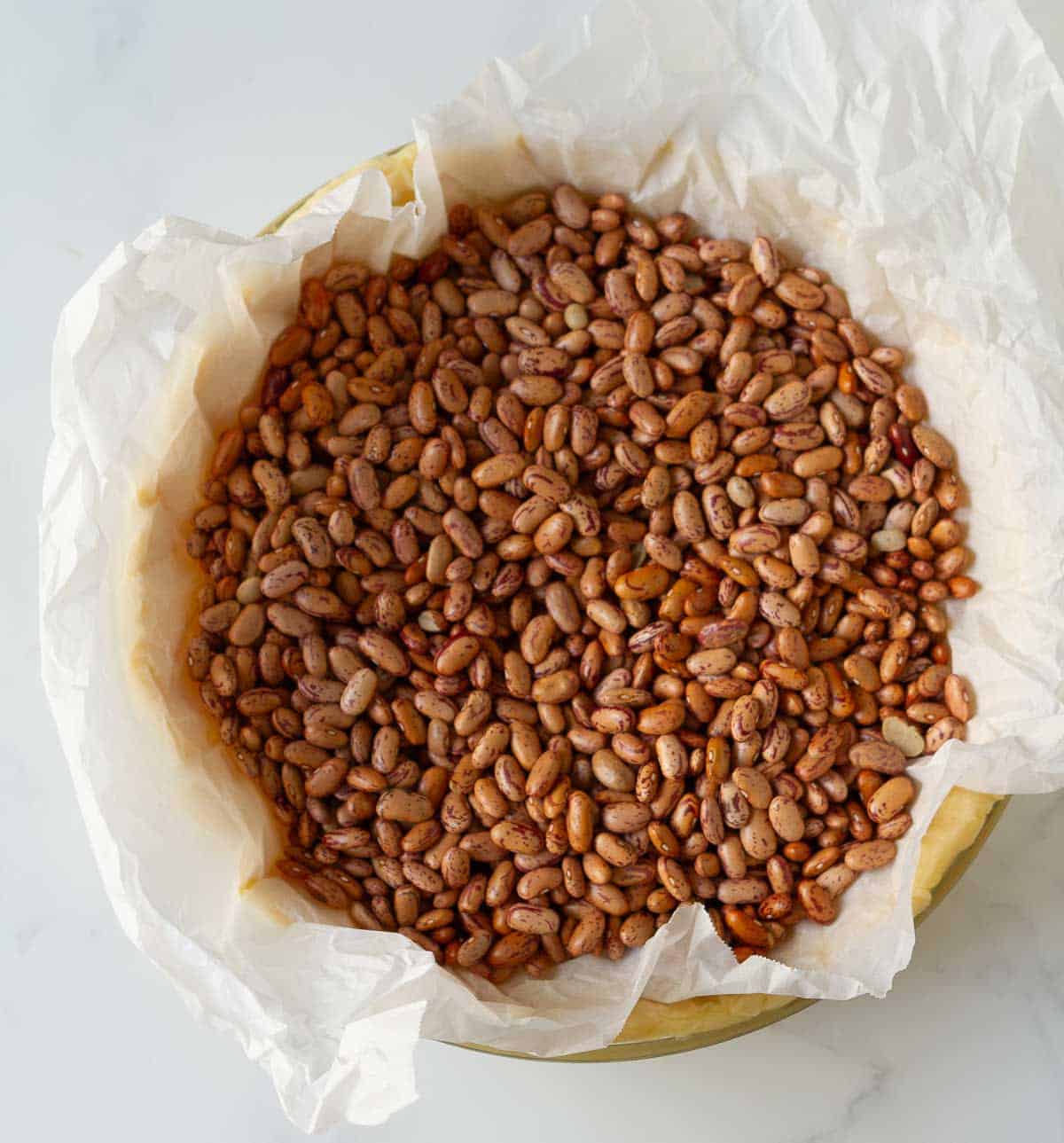 Pie crust in a pie dish covered with parchment paper and red kidney beans.