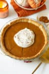 Eggless pumpkin pie with whipped cream on top in a pie dish.
