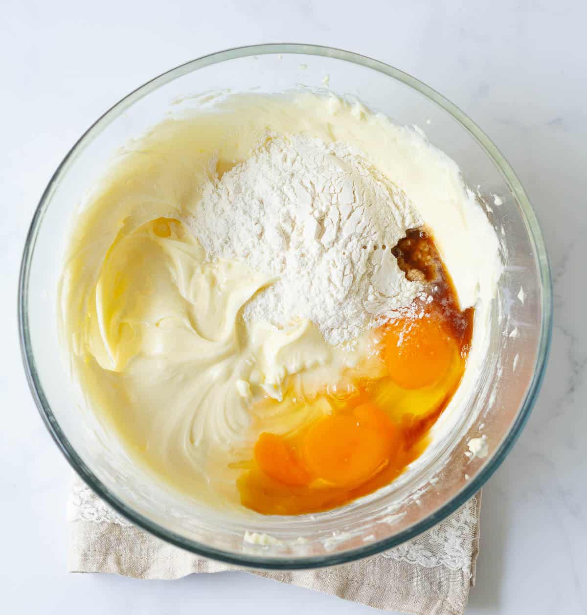 Cream cheese and sugar mixture with eggs, vanilla extract, and flour in a bowl.
