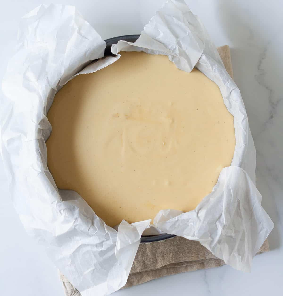 Cheesecake batter in a parchment-lined round cake pan.