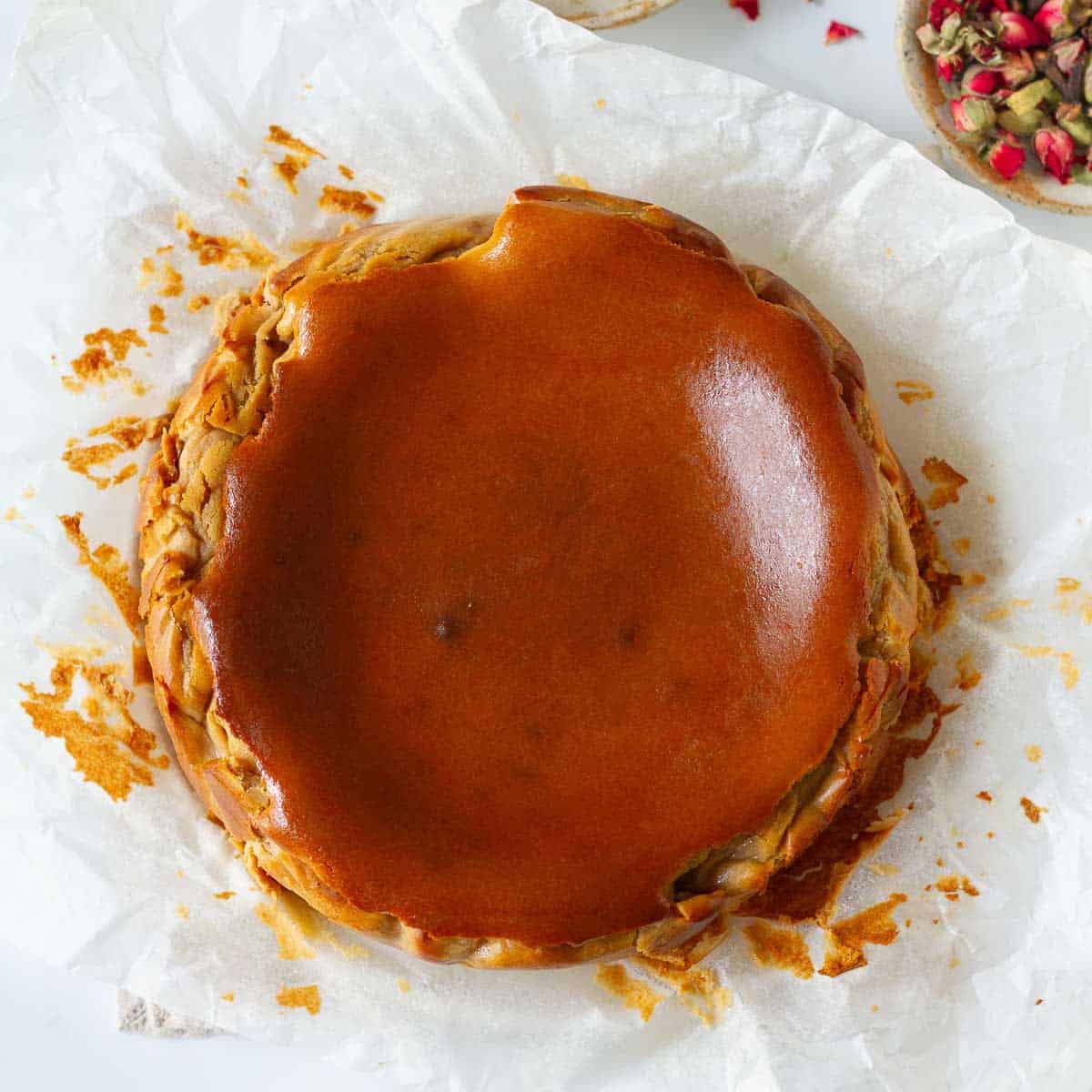 Chai Basque cheesecake on parchment paper with spices in small bowls around it.
